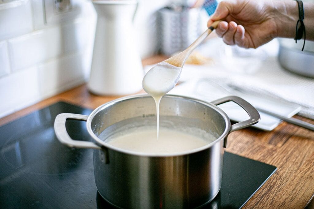 Showing the consistency of besciamella sauce with a wooden spoon.