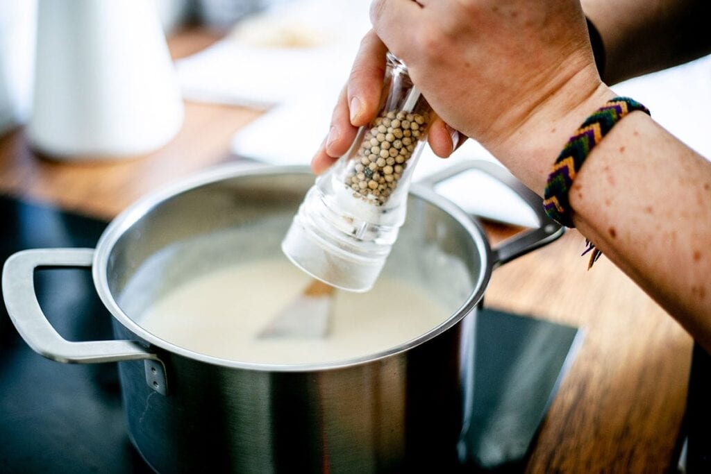 Adding freshly cracked white pepper to the besciamella sauce.