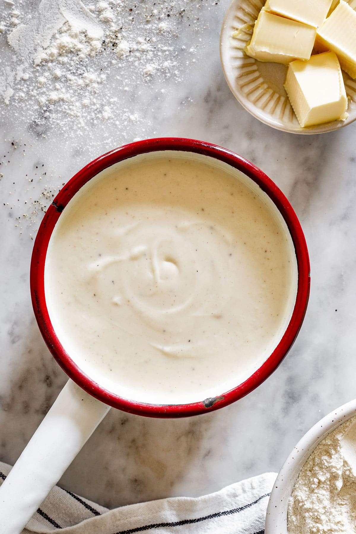 Italian besciamella recipe in a pot with a small plate with butter on the side.