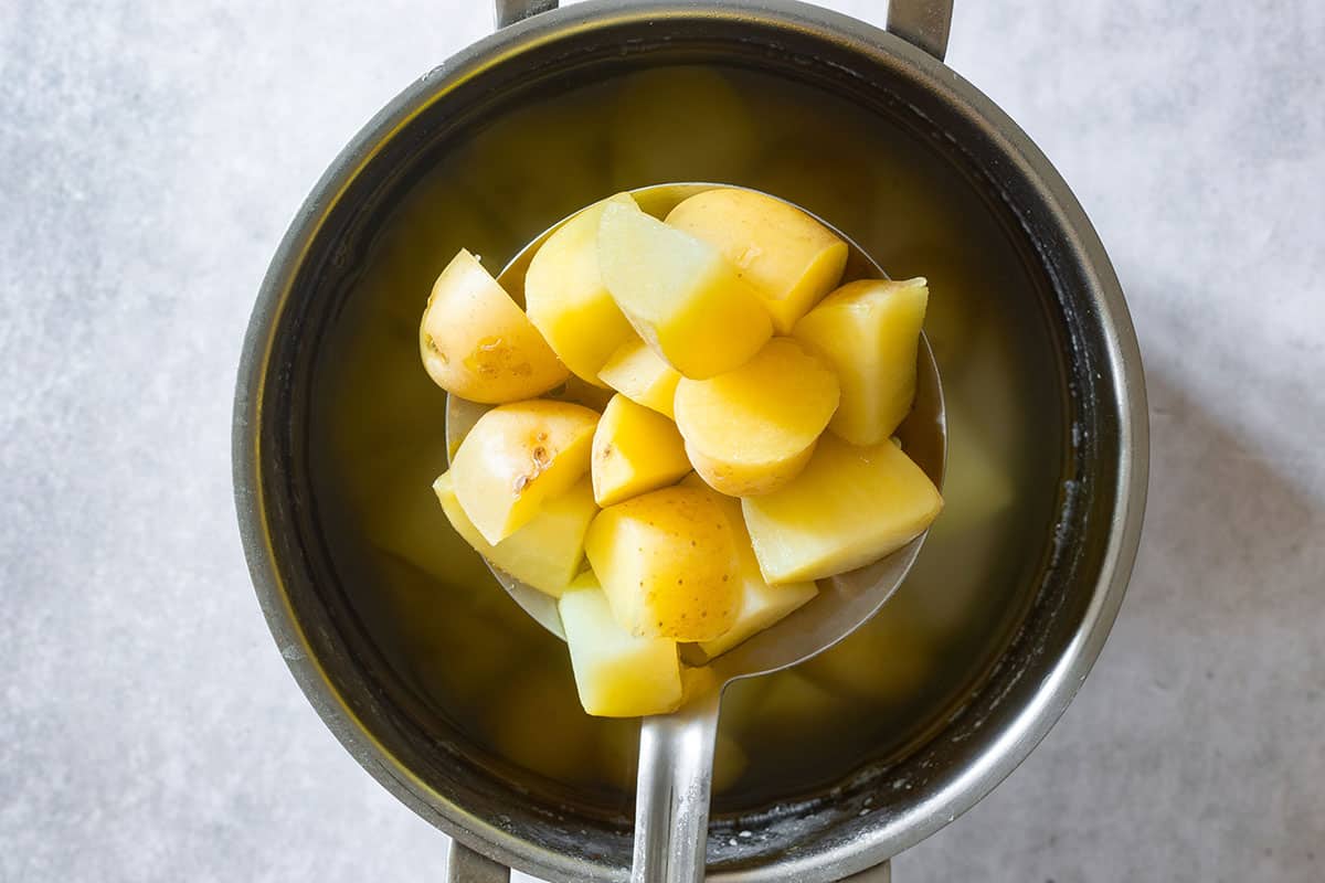 Grabbing cooked potatoes with a slotted spoon from the pot.