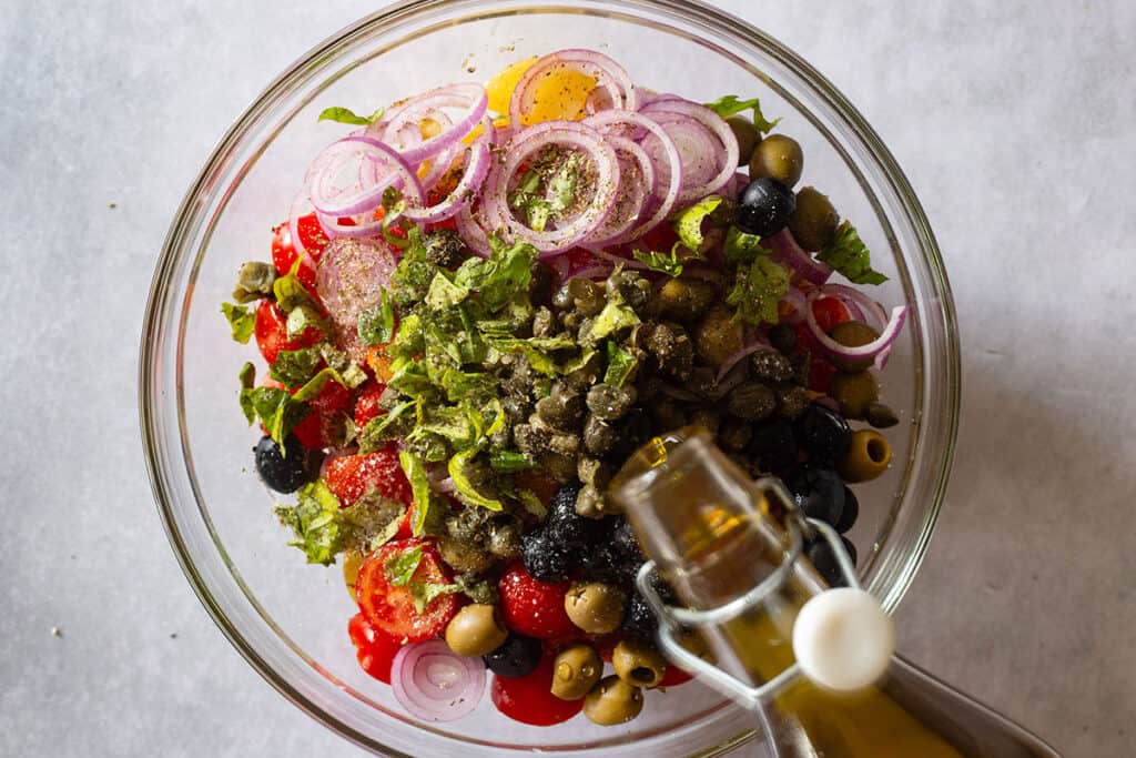 Adding olive oil to the veggies in the bowl.