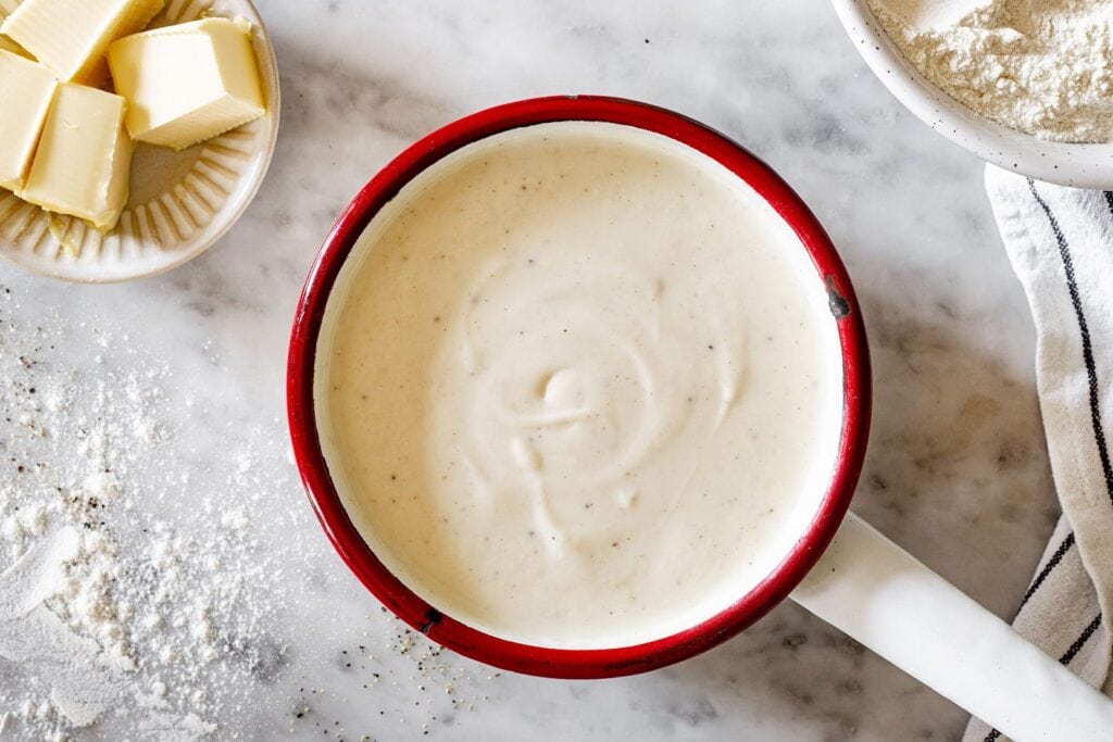 Besciamella recipe sauce in a pot with butter on the side.