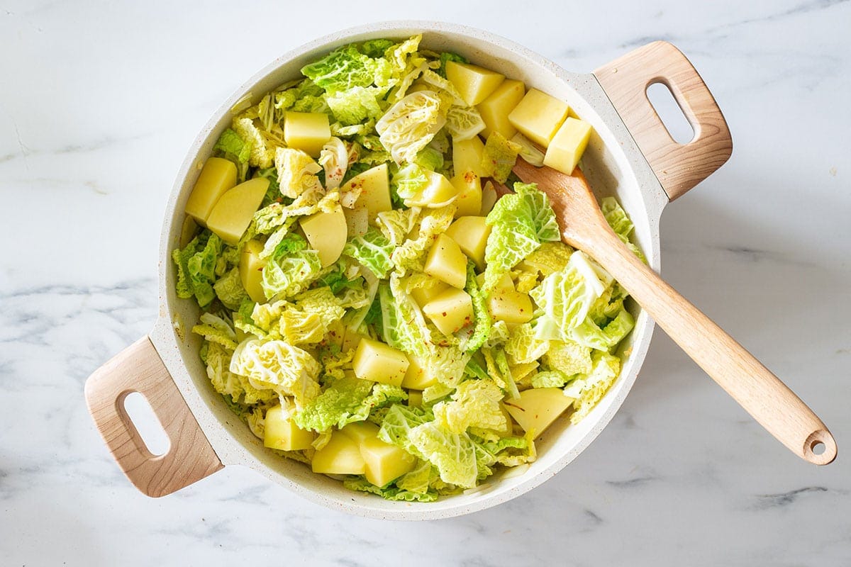 Cabbage and potatoes cooking in a pan.