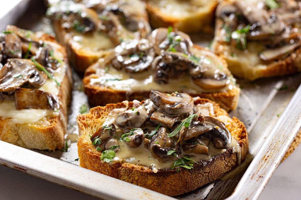 Creamy mushrooms bruschetta with mozzarella (bruschetta con funghi) on a baking tray.