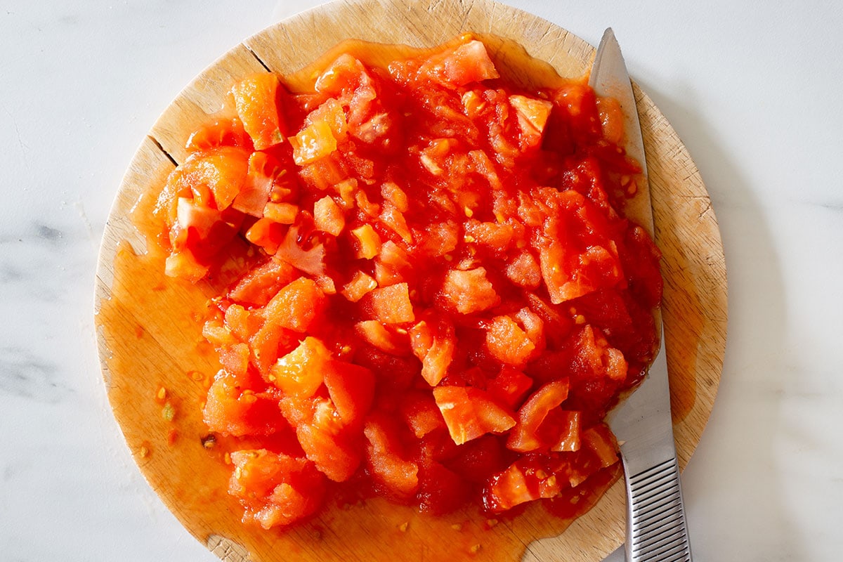 Cooked and chopped tomatoes on a cutting board with a knife on the side.