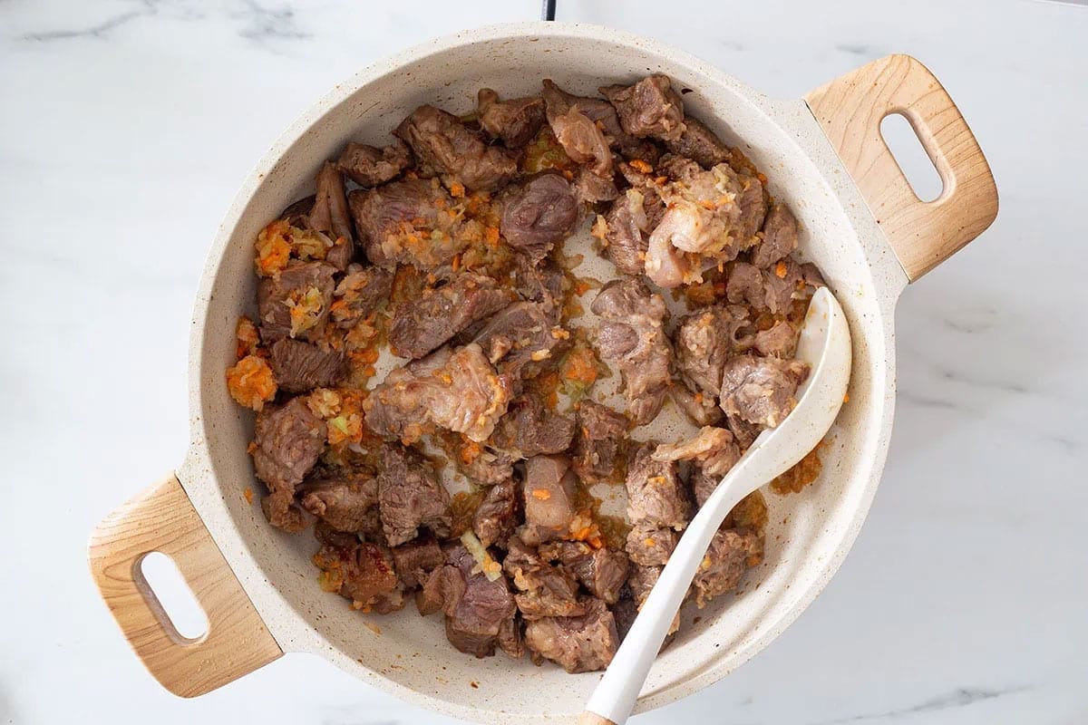 Cooking soffritto with meat chunks in a braising pan.