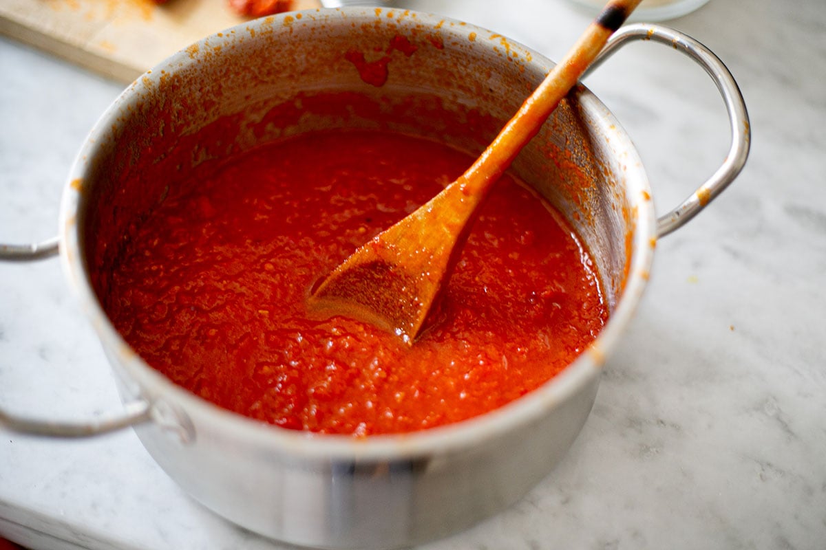 Tomato sauce cooked in a small pot with a wooden spoon.