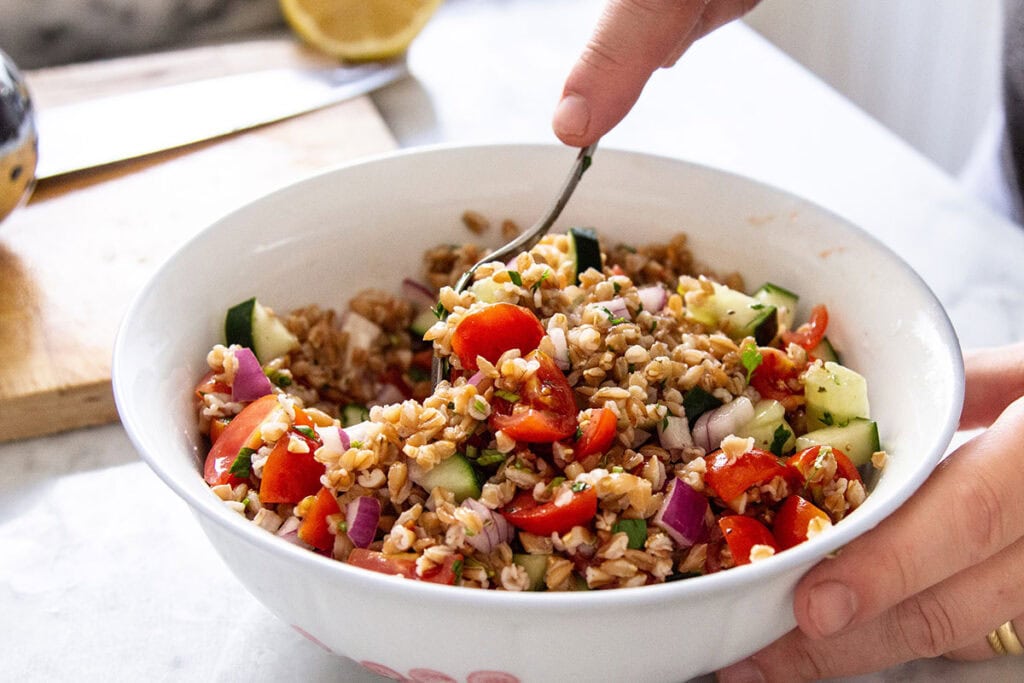 A man mixing the farro salad in a bowl with a spoon.