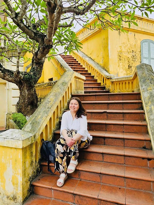 A photo of Mari sitting on stairs with a tree behind.