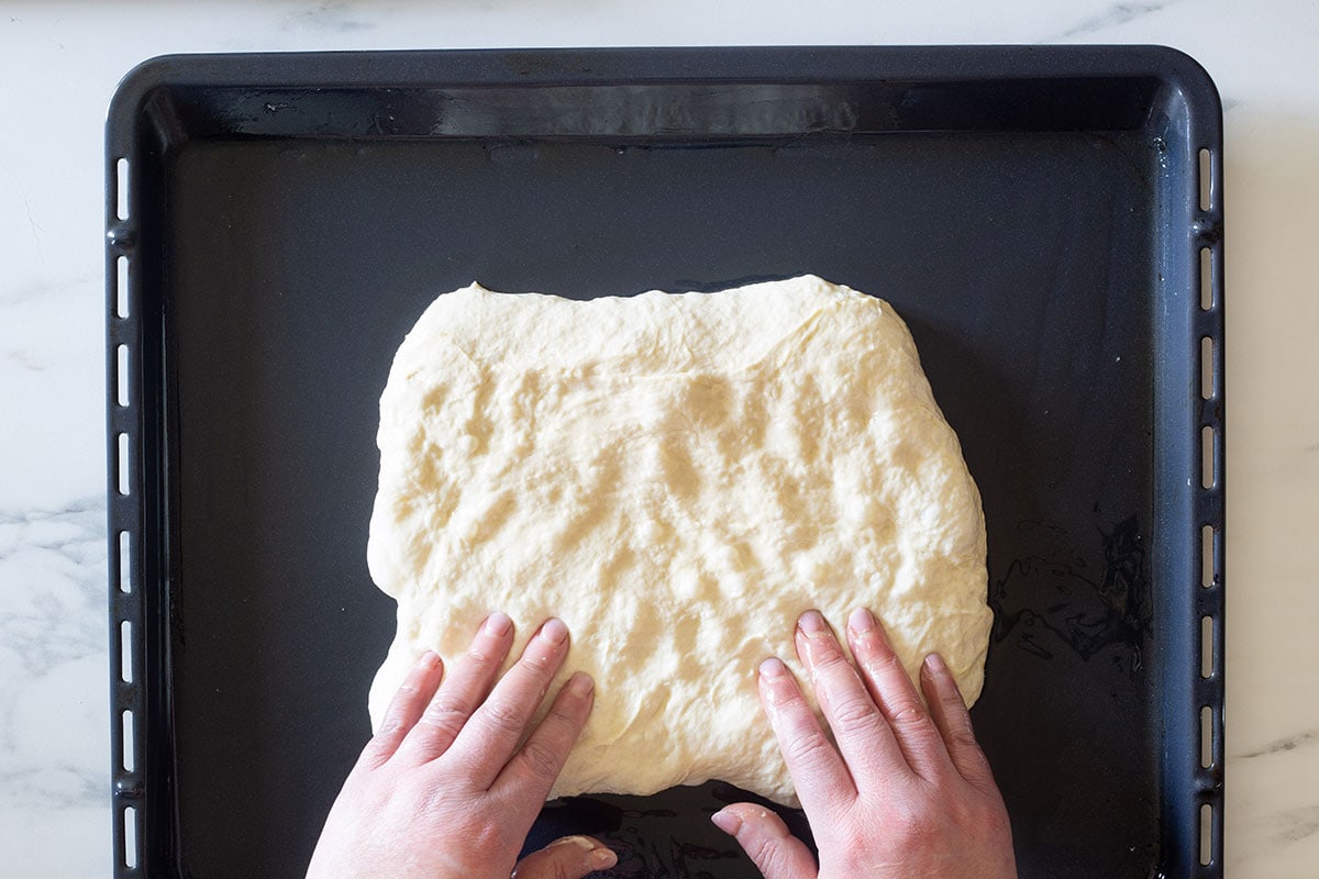Two hands spreading the dough on the middle of a baking sheet.