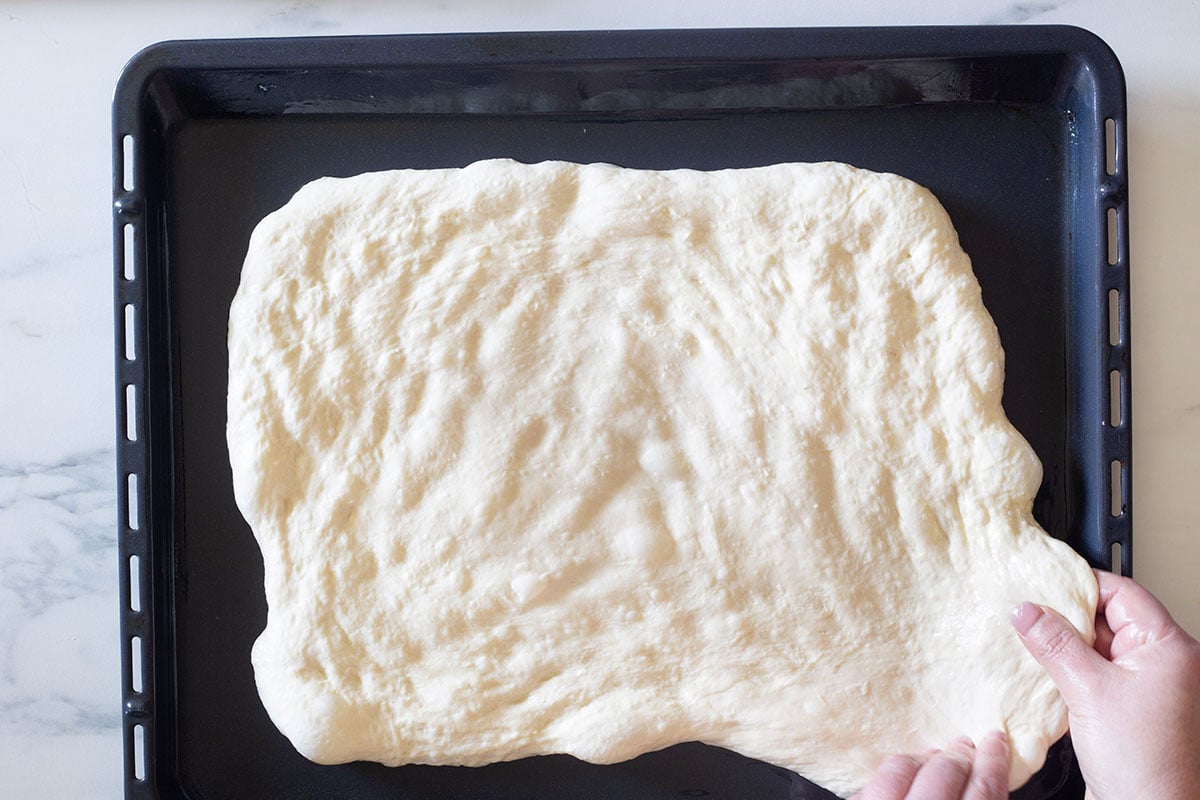 Hands stretching the dough to the ends of a baking sheet.