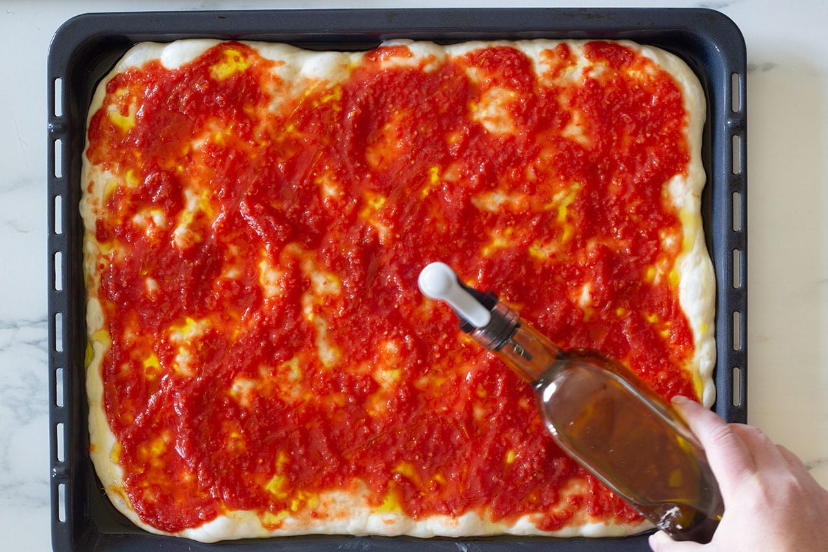 The pizza dough with tomato sauce spread on top and drizzling with olive oil.