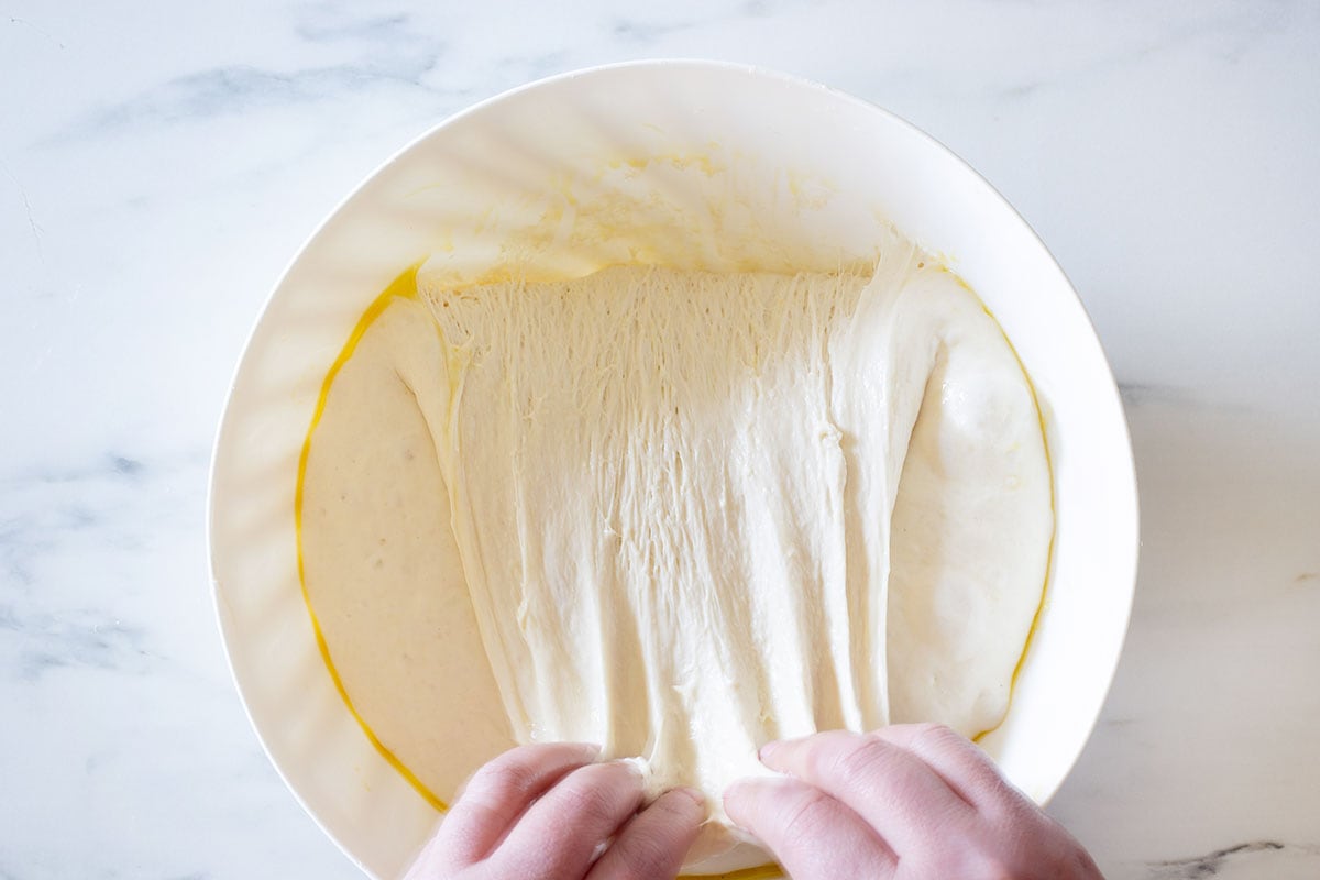 Stretching and folding the raised dough inside the bowl.