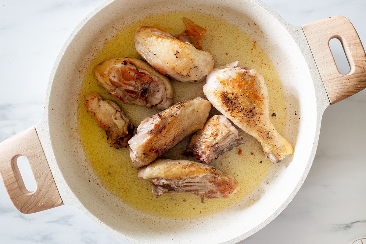 Pieces of chicken browned in a pan.