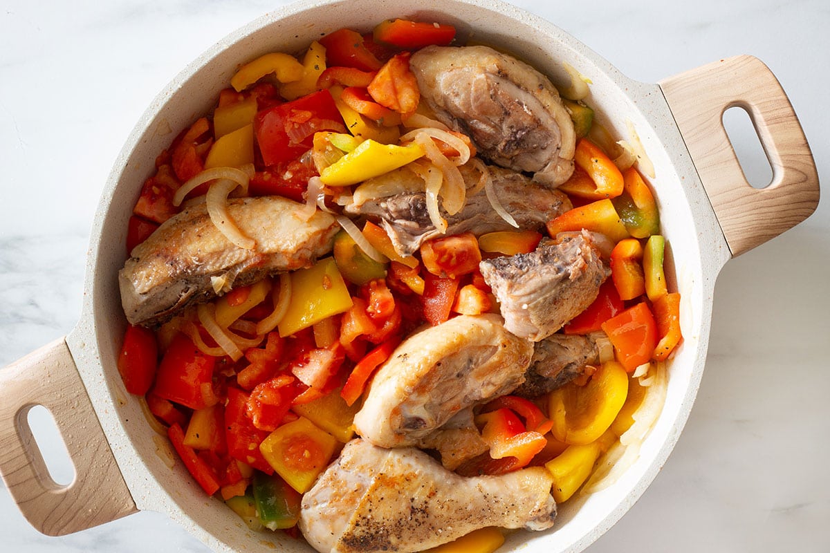 Sautéed peppers and onions mixed with chicken in a pan.
