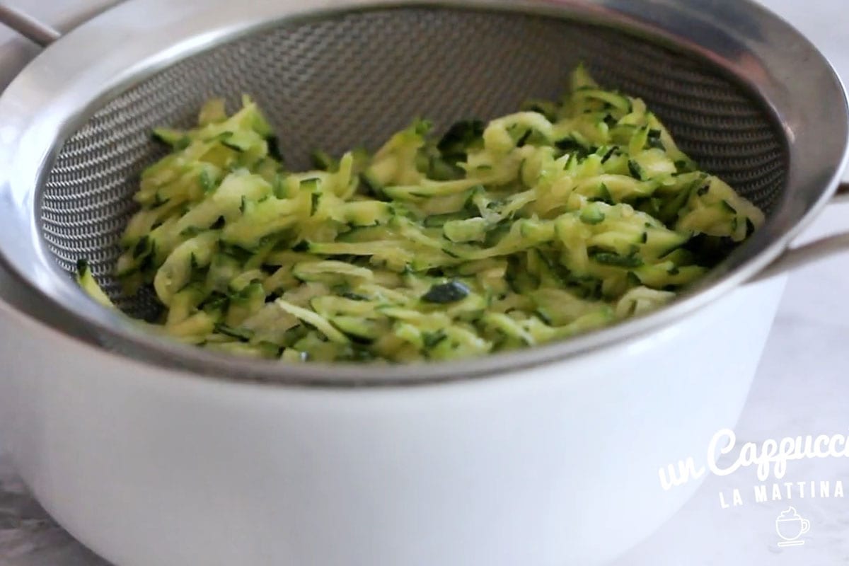 Grated zucchine in a strainer over a bowl.