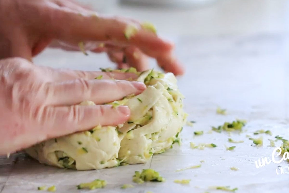 Two hands combining grated zucchini with the dough.