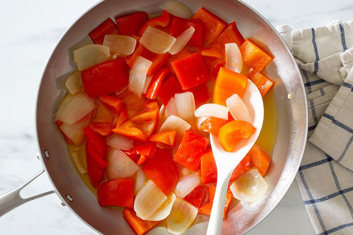 Red bell peppers and onions cooking in a pan.
