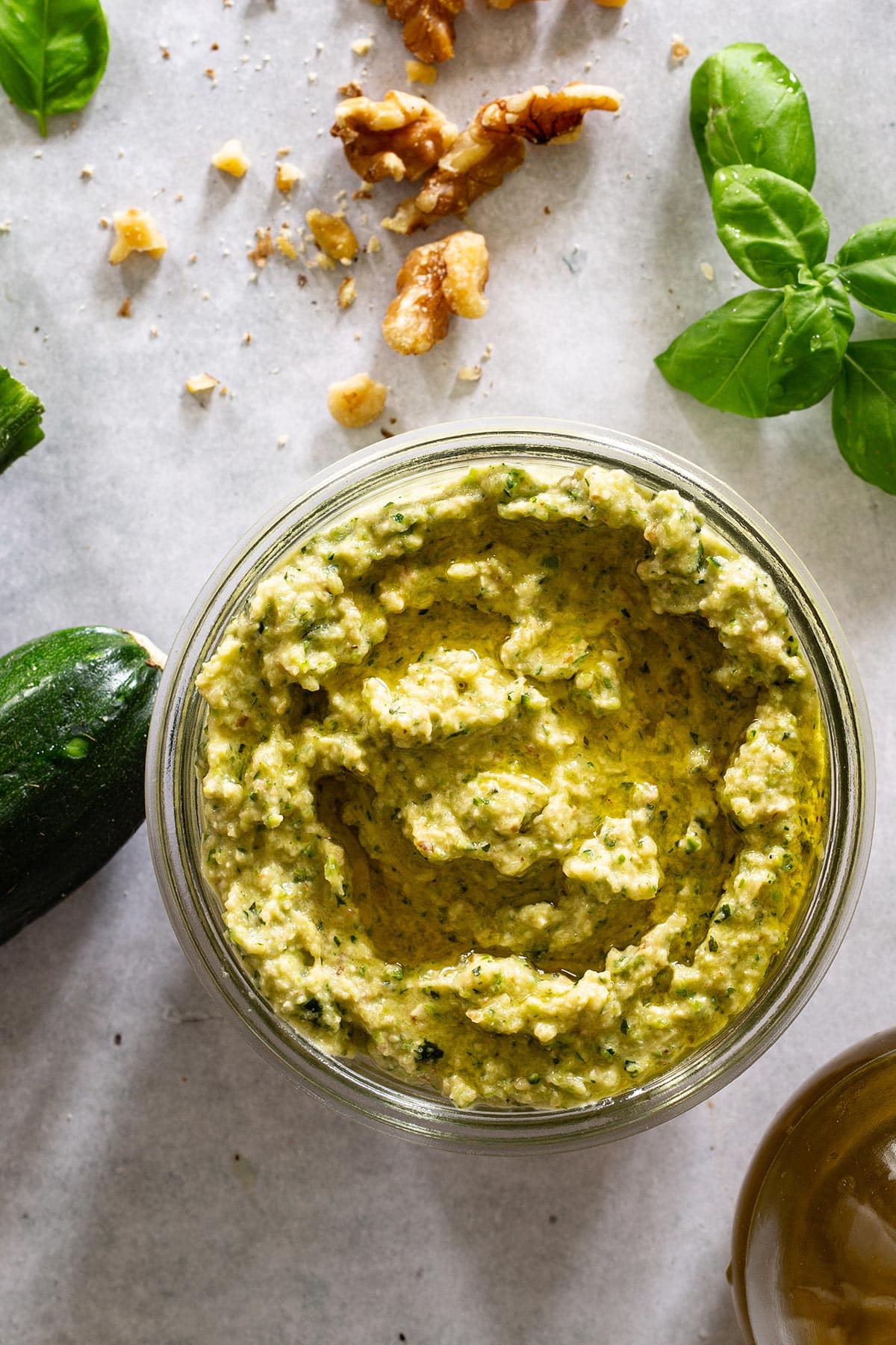 Pesto di zucchine (zucchini pesto) in a jar with some ingredients scattered around.