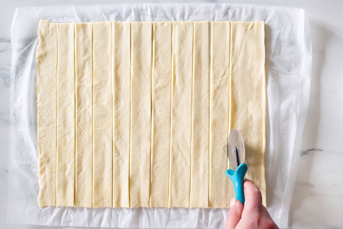 Cutting the puff pastry dough sheet into strips with a pizza cutter.