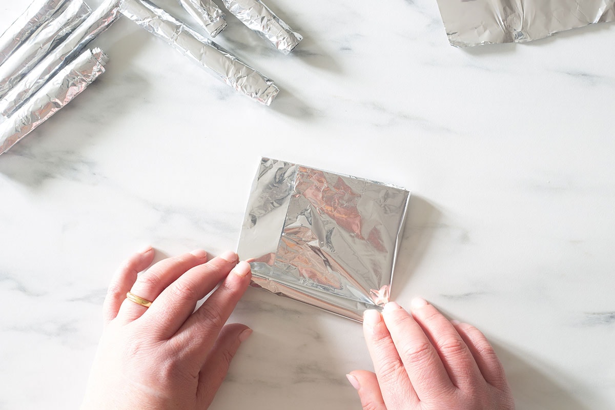 Two woman's hands making cannoncini molds with aluminium  foil.