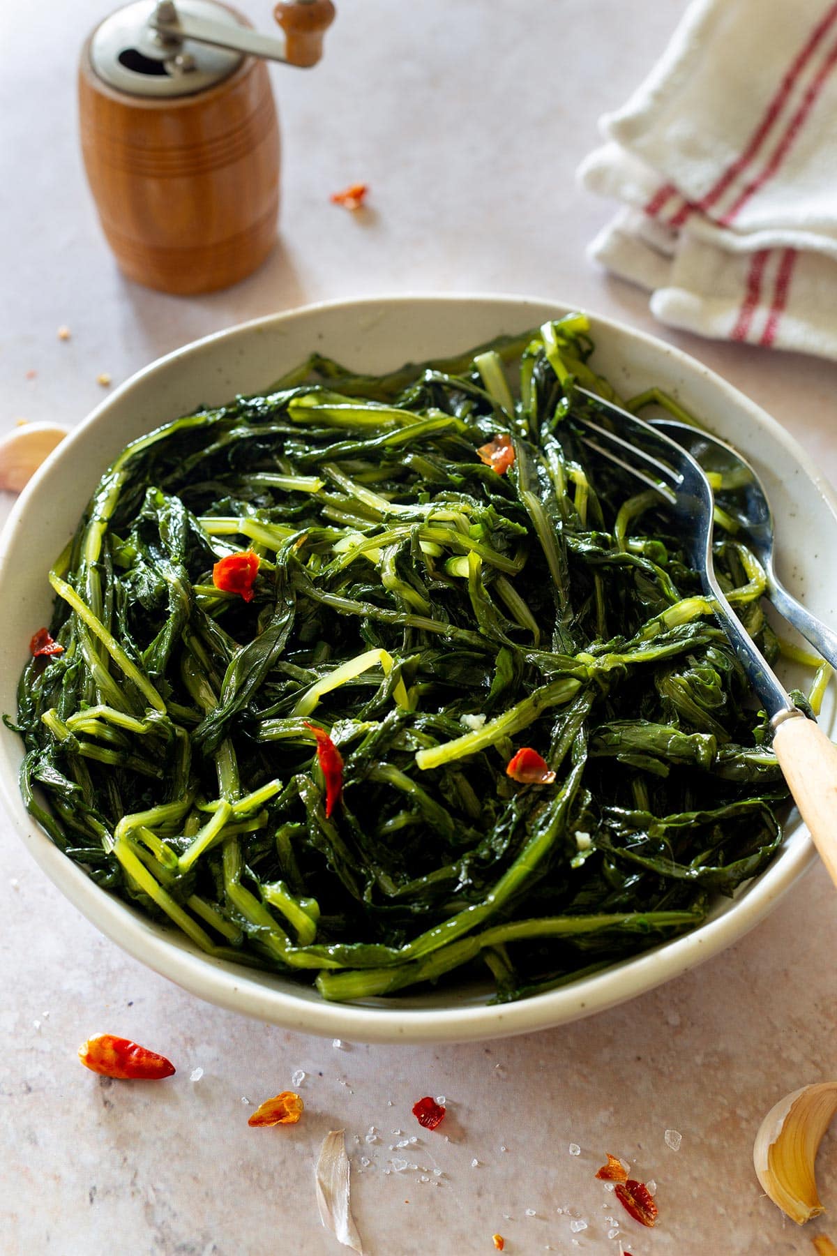 Cicoria ripassata in padella dish, in a bowl with some peperoncino pepper scattered around.