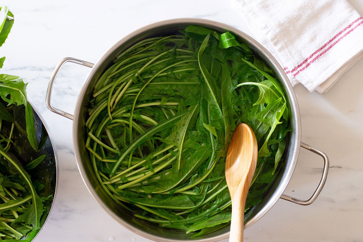 Pushing down the chicory green in boiling water with a wooden spoon.