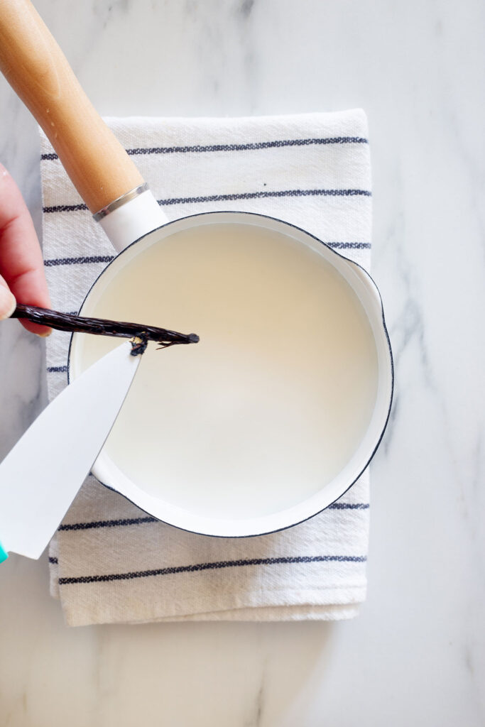 Scrapping a vanilla bean pod with a knife over a pot with milk.
