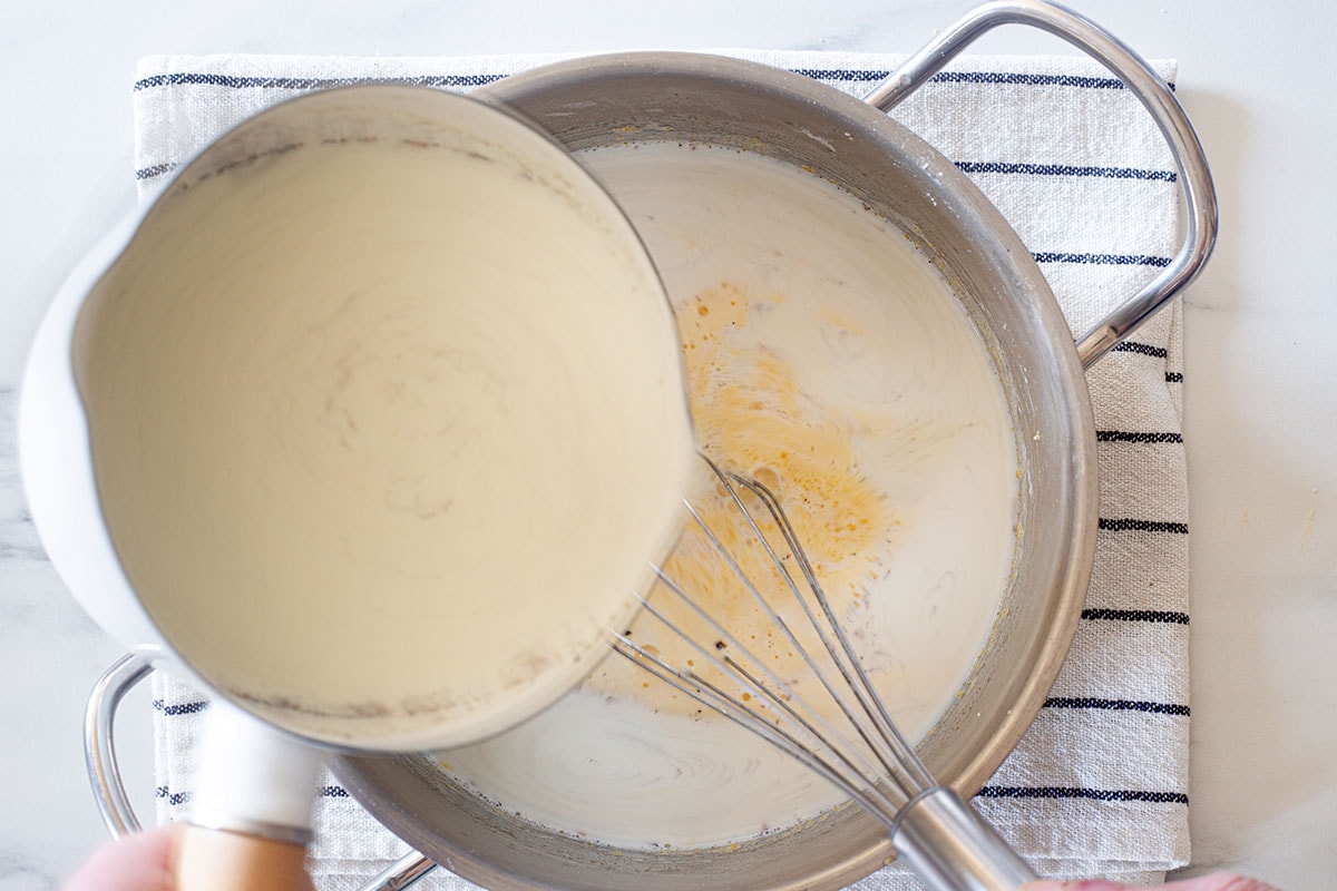 Pouring the hot milk into the pot with the egg yolk mixture.
