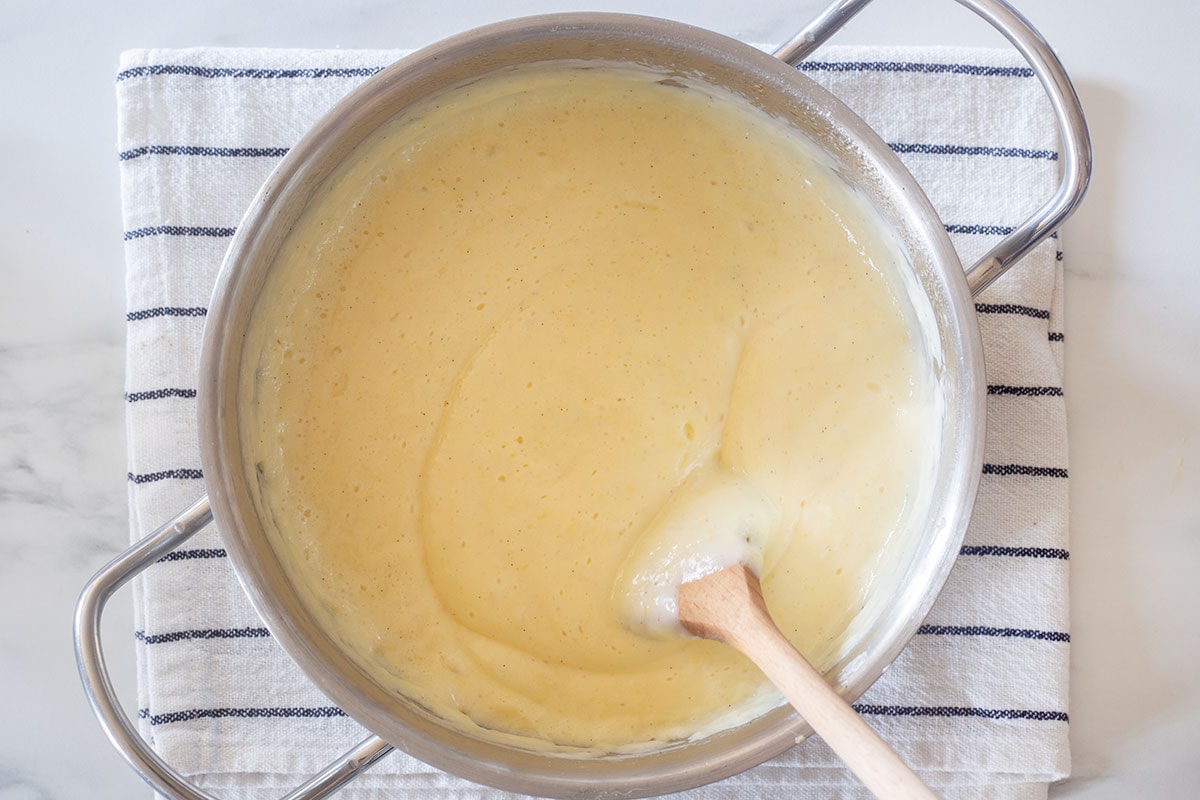 Cooking the Italian pastry cream in a pot with a wooden spoon.