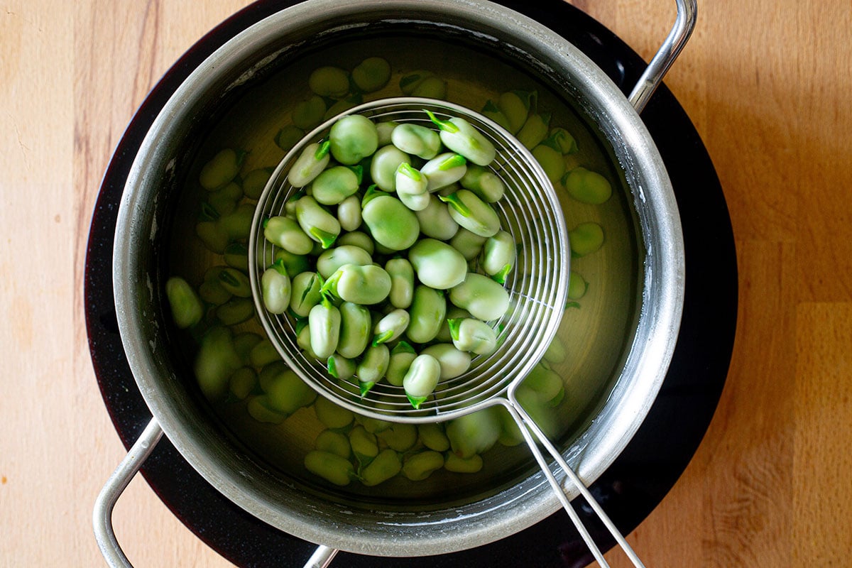 Taking blanched fava beans with a slotted spoon from the pot.