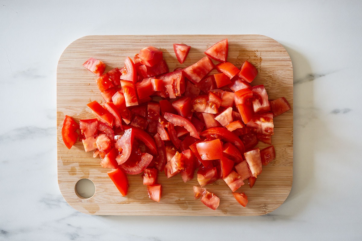 Fresh tomatoes cut into chunks on a cutting board.
