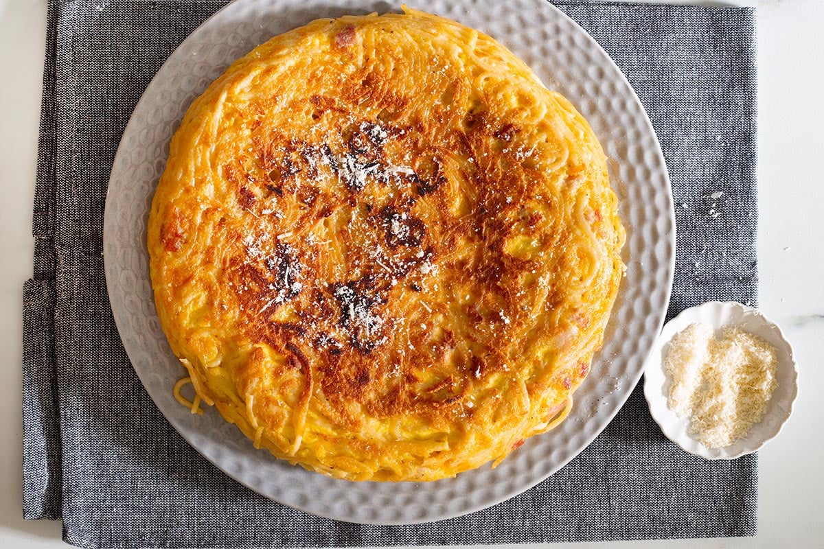 Spaghetti frittata in a platter, served with a sprinkle of parmigiano cheese on top.