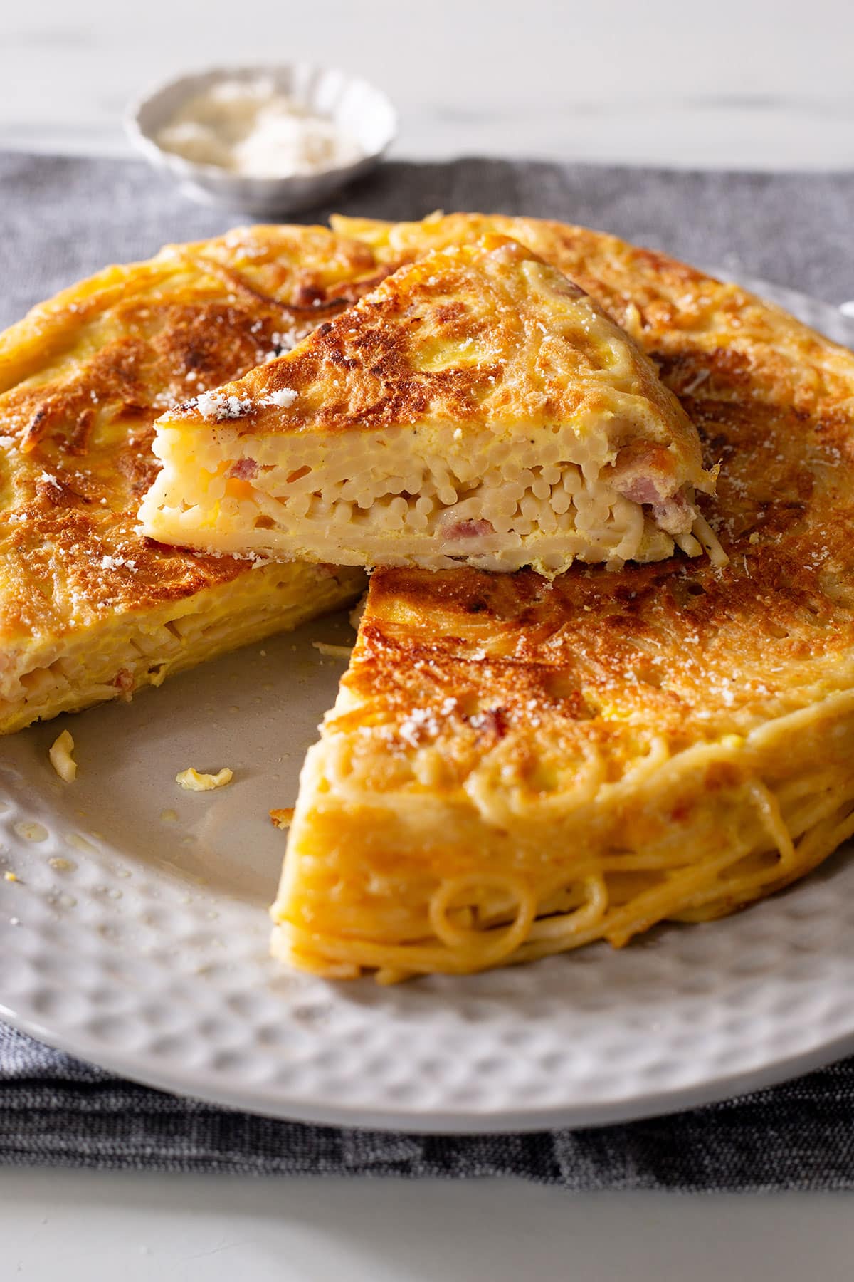 Frittata di spaghetti in a plate with a portion cut and placed on top.