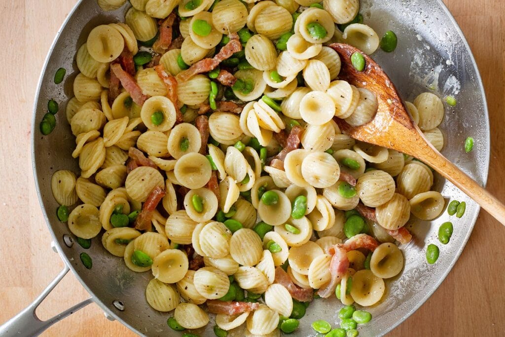 Pasta with fave and guanciale in a pan.