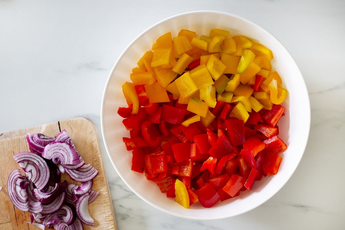Bell peppers cut into small squares in a bowl, and the onion sliced on a cutting board.