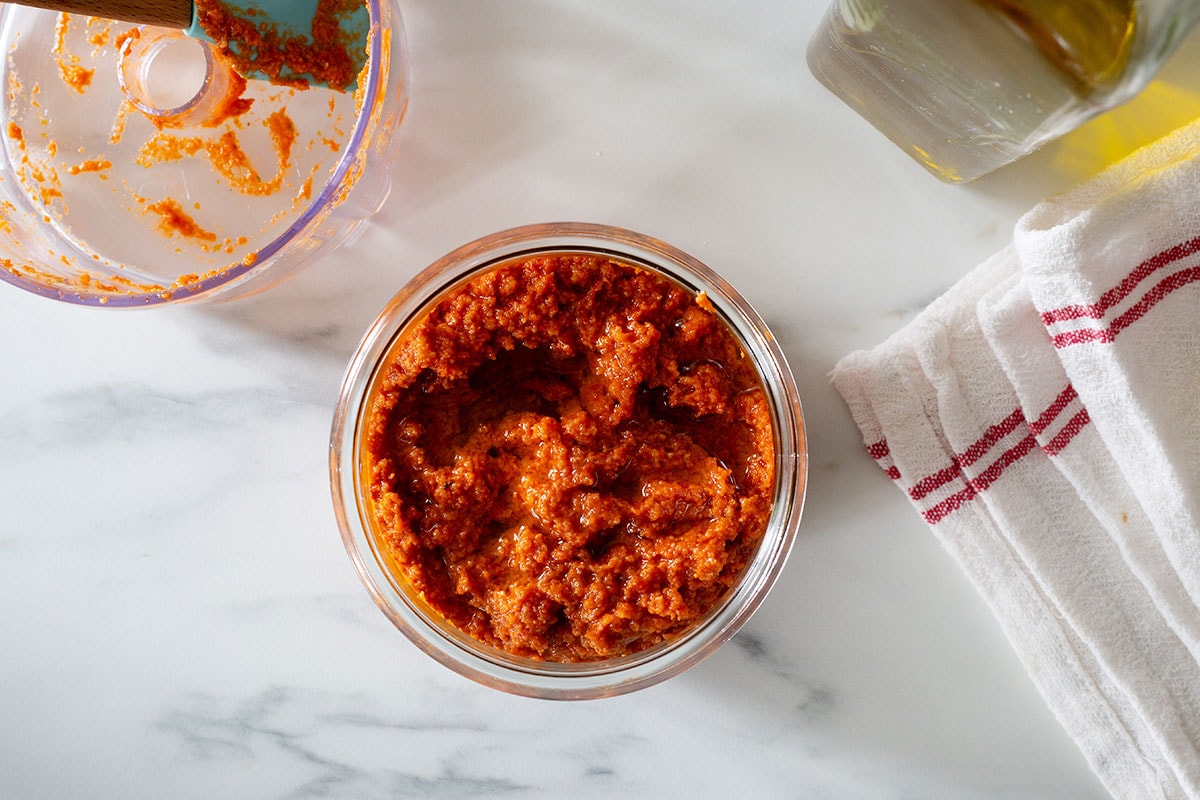 Pesto con pomodori secchi in a jar, an olive oil bottle on the side and the empty food processor on the other side.