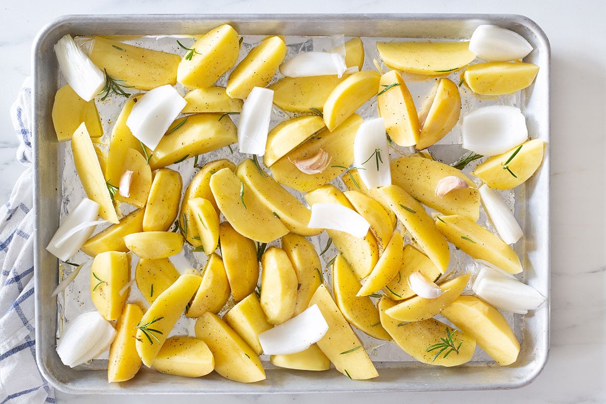 Potatoes and onion wedges on a tray with garlic and rosemary.