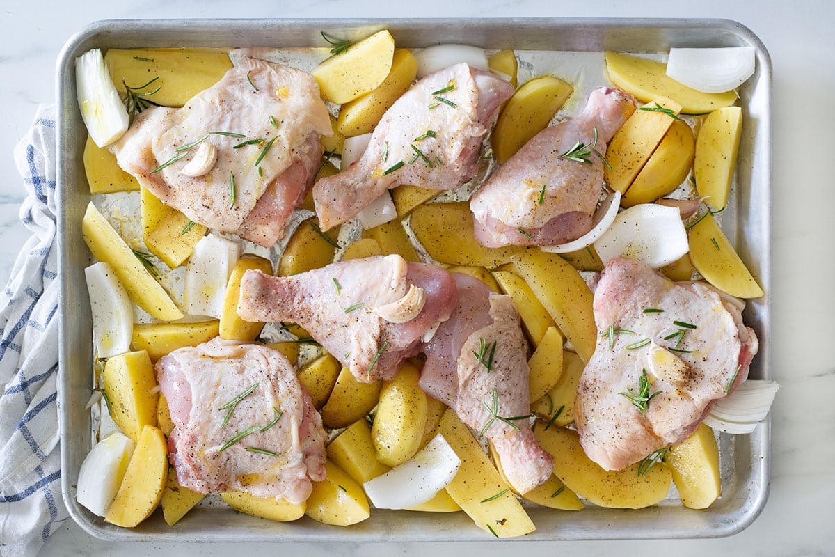 Chicken and potatoes mixed with onion, garlic, and rosemary ready on a baking tray.