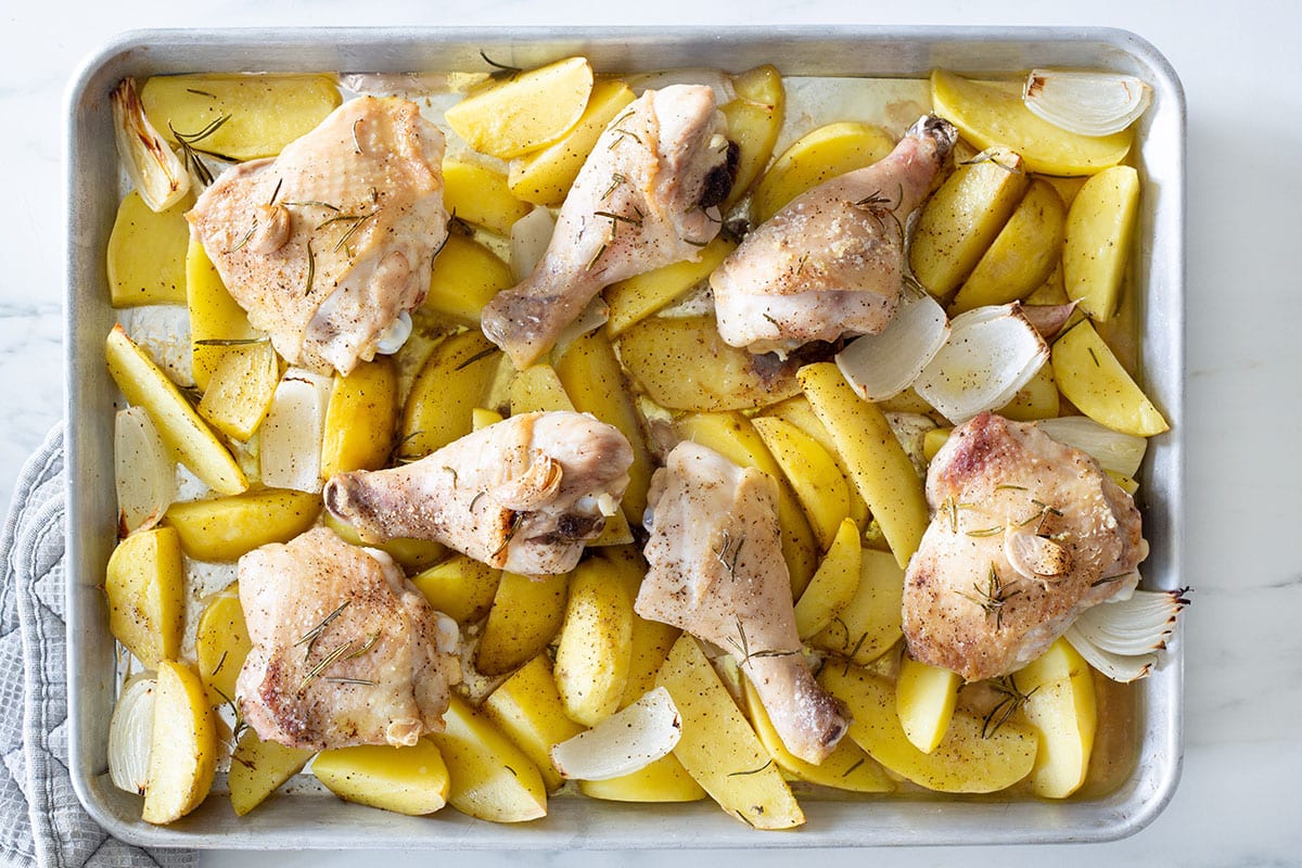 Half baked chicken and potatoes in a tray.