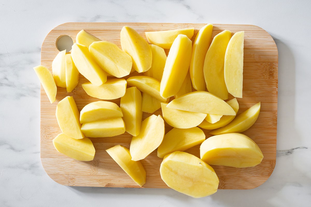 Potatoes peeled and cut into wedges on a cutting board.