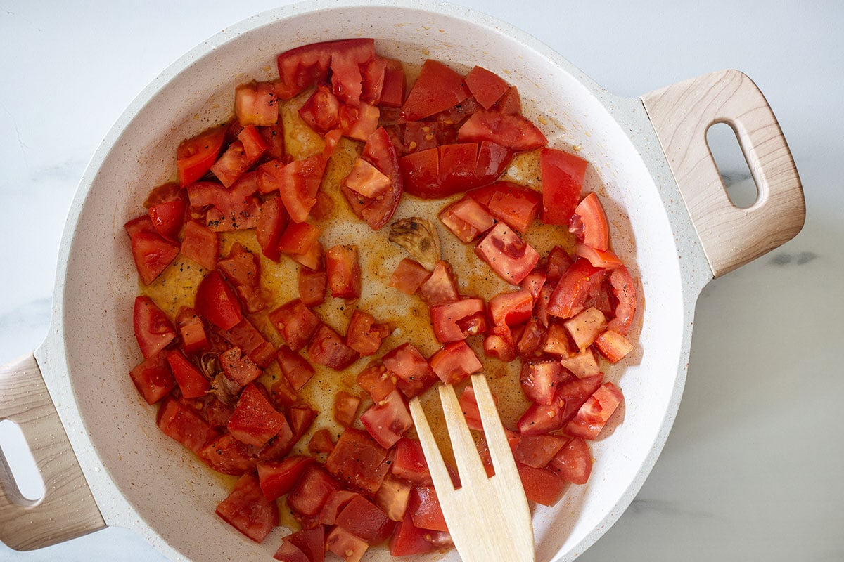 Tomato chunks in a pan with garlic and seasoned with salt and pepper.