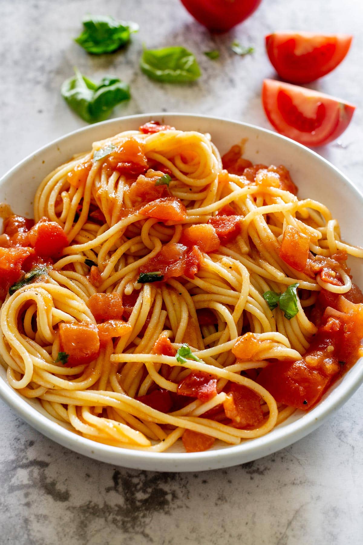 Spaghetti al pomodoro fresco in a plate with fresh tomatoes on the background.