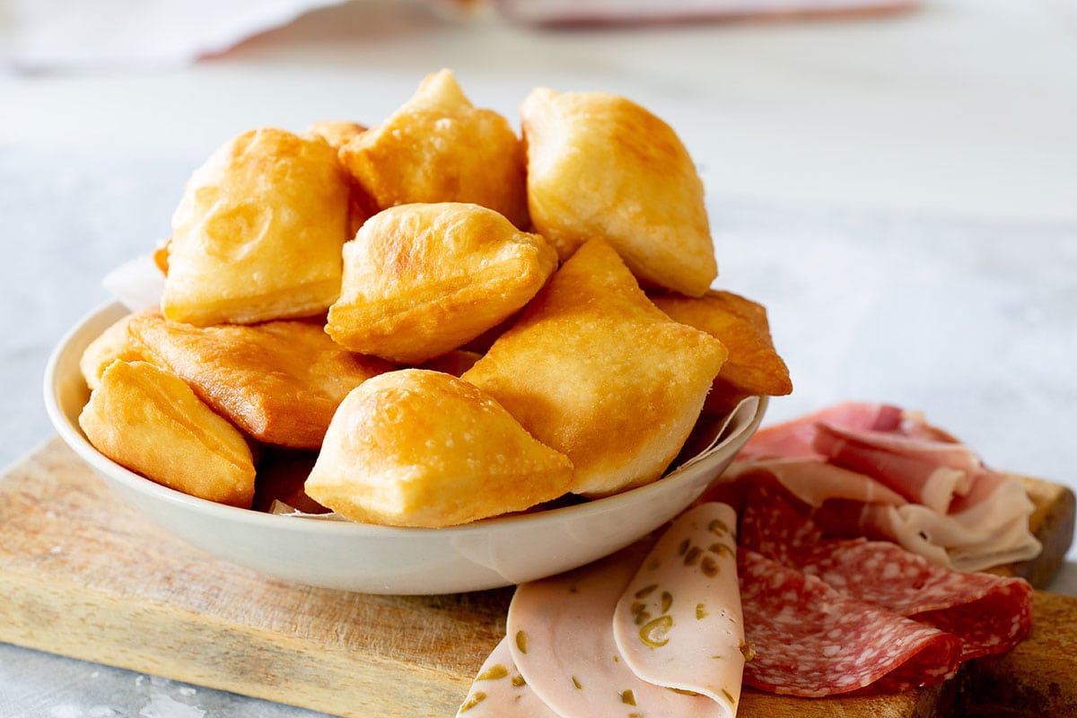 Torta fritta, also known as gnocco fritto on a cutting board with cured meats.