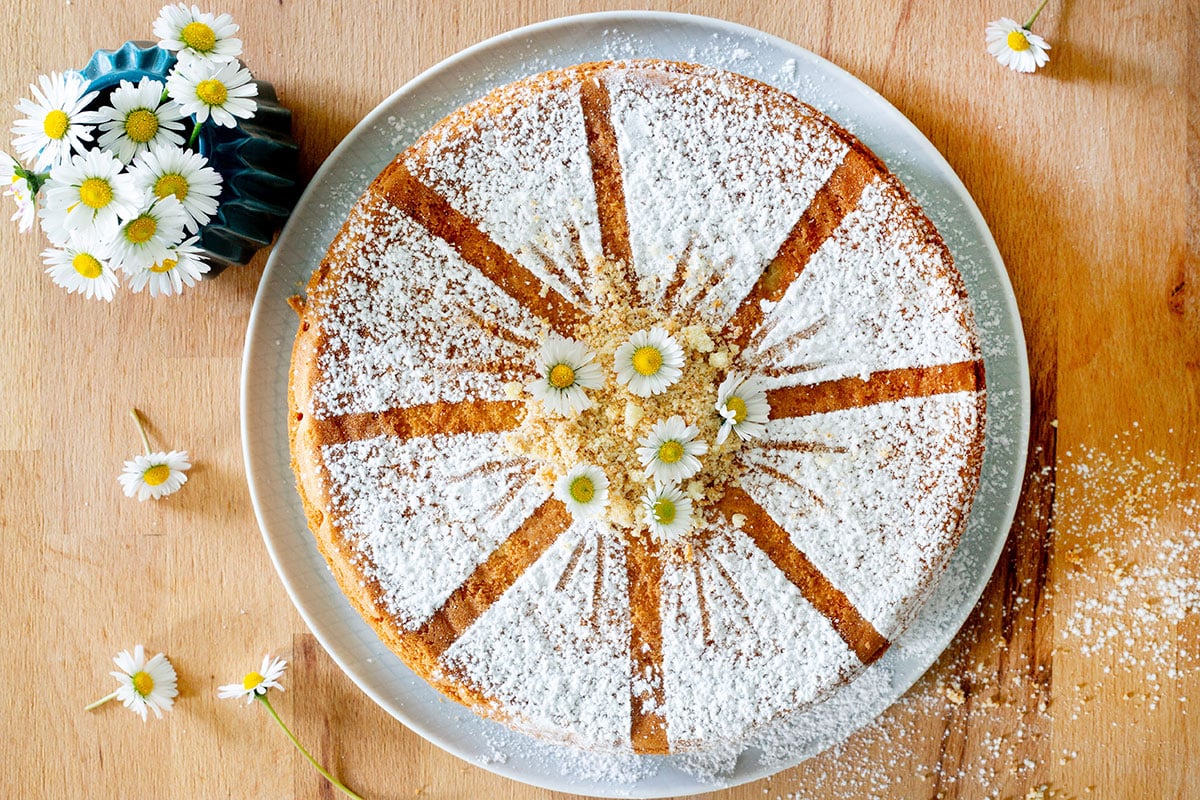 A beautiful Torta Margherita sponge cake decorated with fresh daisies on top.