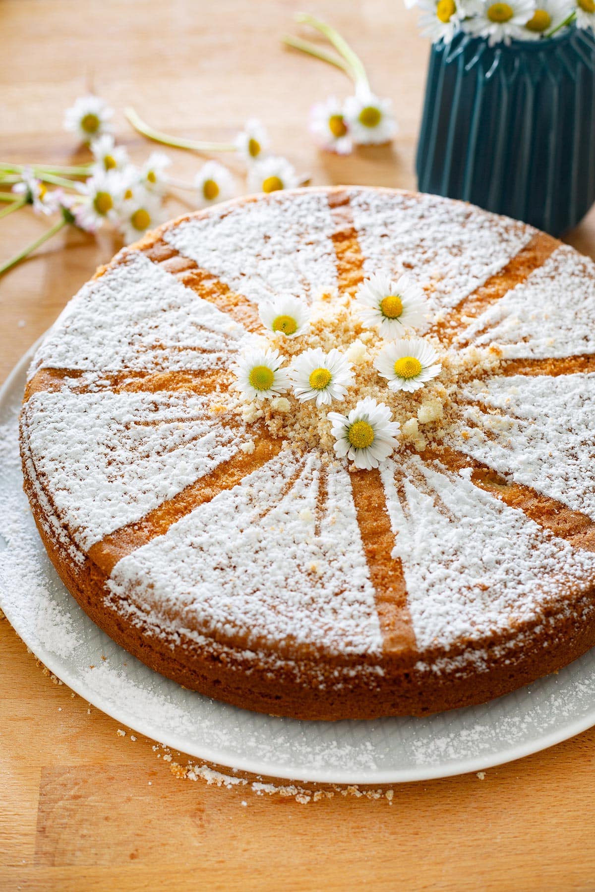 Torta Margherita (Italian sponge cake) on a platter and decorated with some fresh daisies on top.