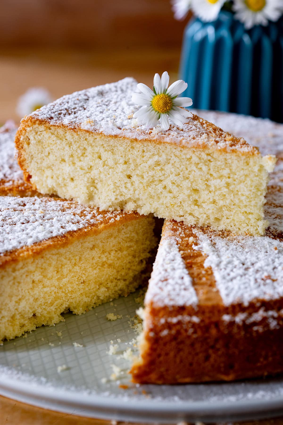 Torta margherita with a slice cut and placed on top with a daisy as decoration.