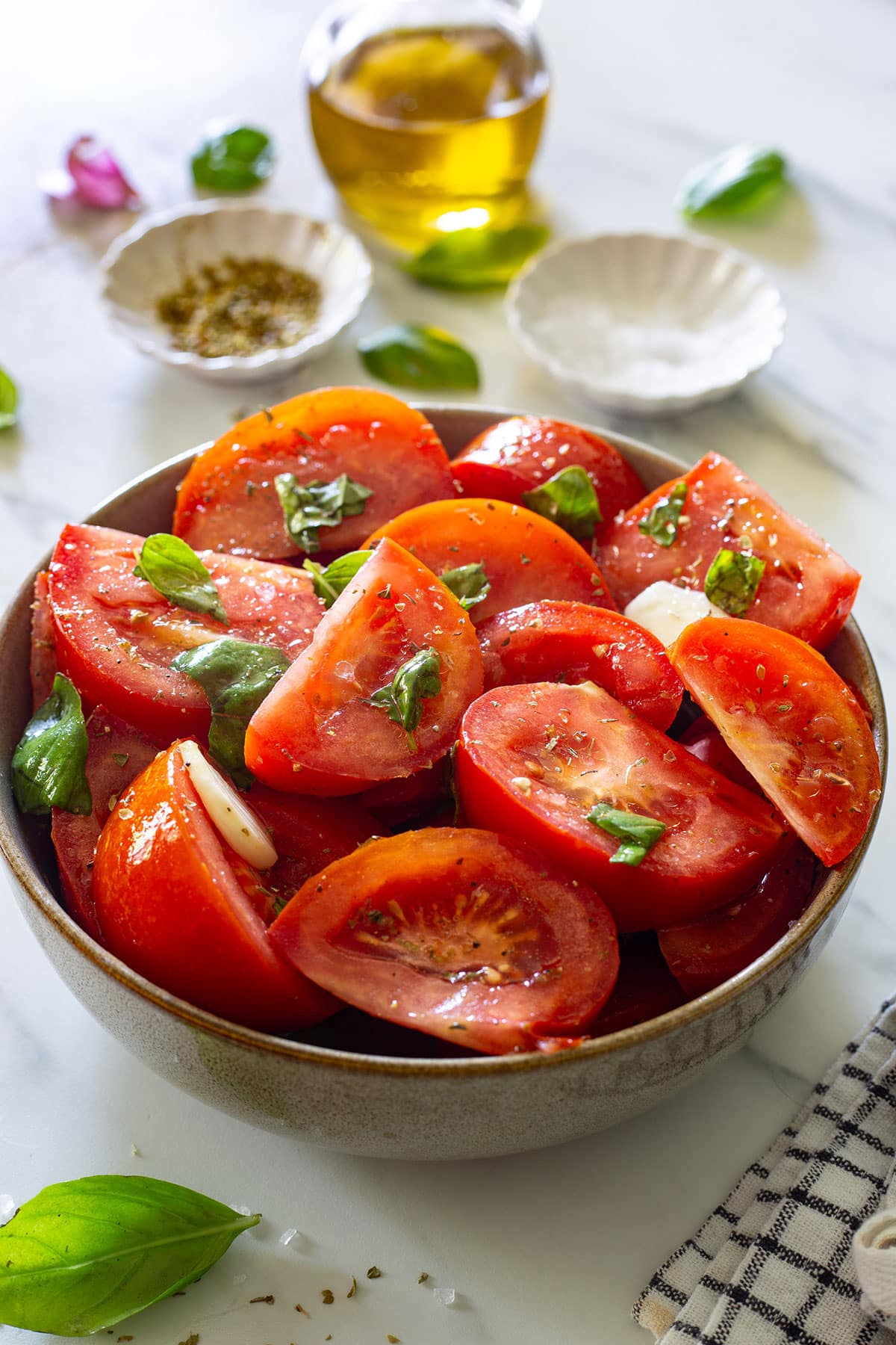 A classic Italian tomato salad, Insalata di Pomodori, in a bowl with some ingredients in the background.