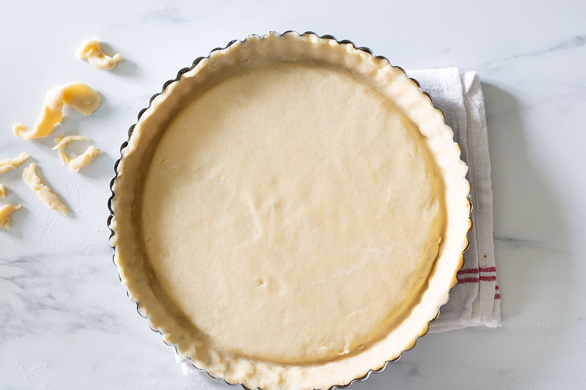 The dough arranged inside the tart pan with the excess of dough trimmed.