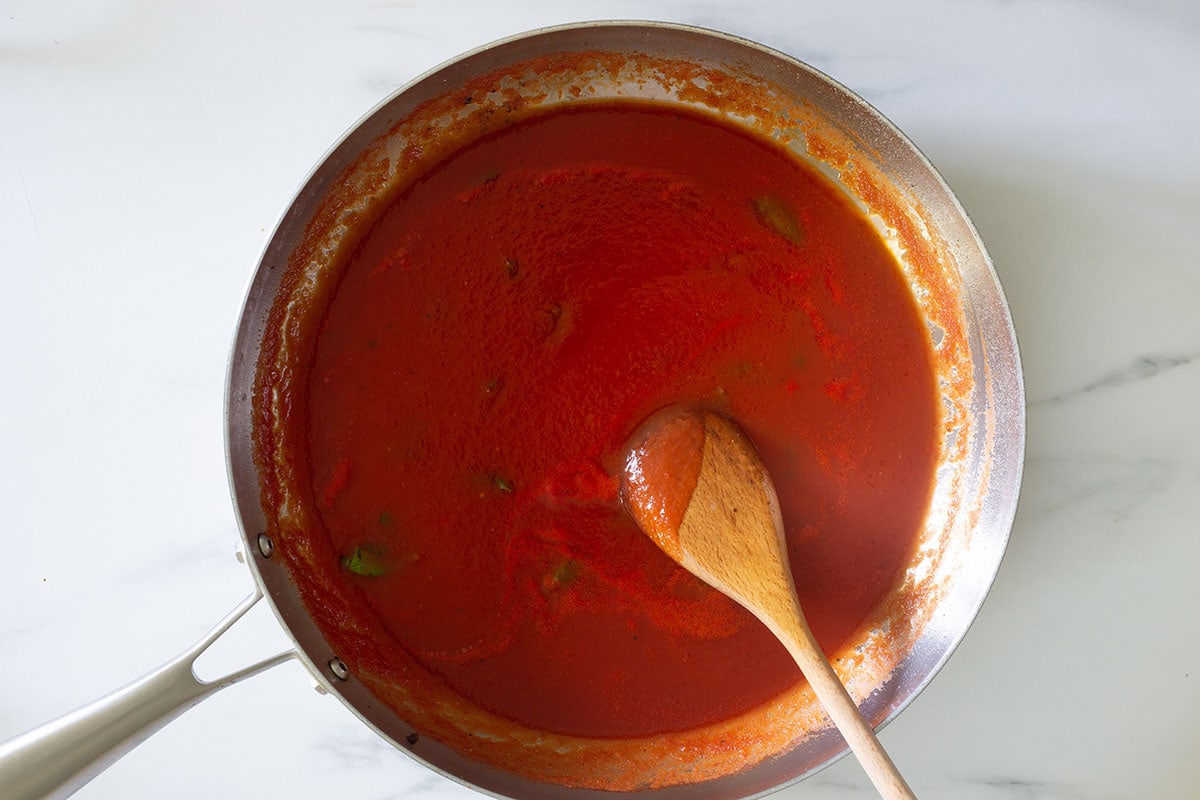 Tomato sauce with basil in a pan with a wooden spoon.